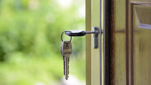 Blick ins Grüne durch eine offene Haustür, in der ein Schlüssel steckt