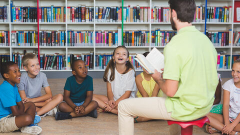Erziehung und Lernen (Symbolbild) Kinder in einer Bücherei, ein Mann liest ihnen vor