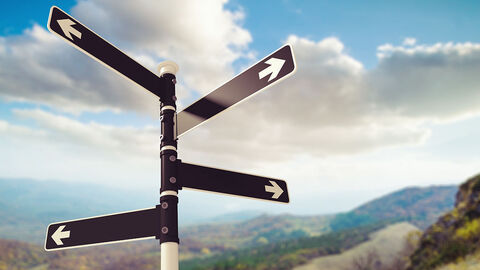 Pfahl, an dem vier Schilder in verschiedene Richtungen weisen, dahinter Berge