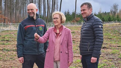 Eine Frau steht zwischen zwei Männern auf einem Feld und hält eine kleine Wurzel in der Hand.