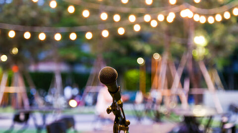 Kulturelle Veranstaltungen (Symbolbild) Im Vordergrund ein Mikrofon, dahinter verschwommen Tische, Stühle und Lampions