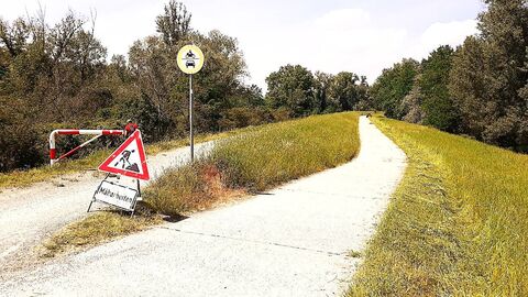 Ein Warnschild steht neben einem Deichpfad und weist auf die laufenden Mäharbeiten auf dem Deich hin.