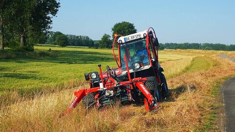 Ein Mähtraktor fährt auf einem Deich und mäht das hohe Gras.