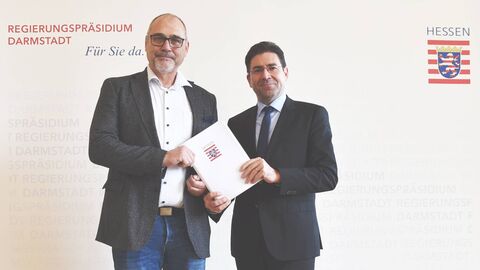 Zwei Männer vor weißem Hintergrund mit Papier in der Hand