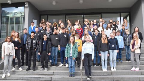 Eine große Gruppe von Kindern und Jugendlichen steht auf einer großen Treppe vor einem Gebäude für ein Foto bereit.