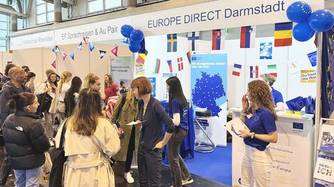 Viele junge Menschen stehen vor einem Messestand und unterhalten sich.