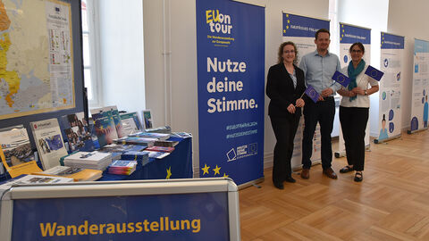 Wanderausstellung zur Europawahl Tische mit Infomaterial, Roll-ups, davor drei Personen