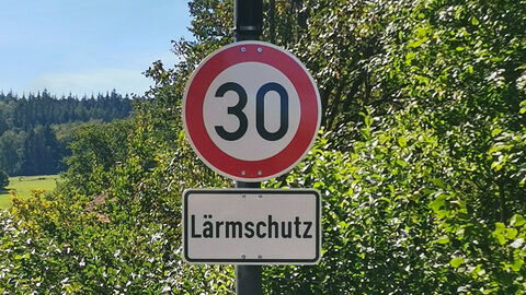 Tempo 30-Schild mit dem Zusatz „Lärmschutz“, dahinter Bäume und Felder