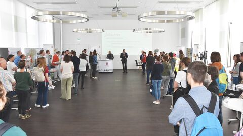 RP-Jobmesse Viele junge Menschen stehen in einem großen Saal und blicken nach vorne auf einen Mann, der ein Mikrofon in der Hand hält und zu ihnen spricht.