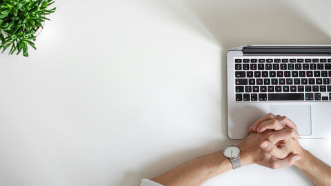 Entscheidungen (Symbolbild) Person mit gefalteten Händen vor einem Laptop