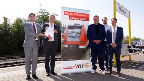 Drei Männer stehen an einem Bahnsteig und blicken in die Kamera. Ein Mann übergibt einem anderen Mann eine Urkunde. Die anderen drei Männer stehen daneben.