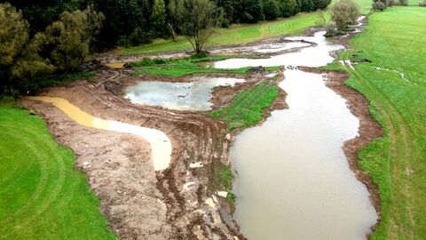 Die Baustelle am Seemenbach nach den jüngsten Regenfällen Bachlauf mit Erdarbeiten am Rande, daneben grüne Wiese