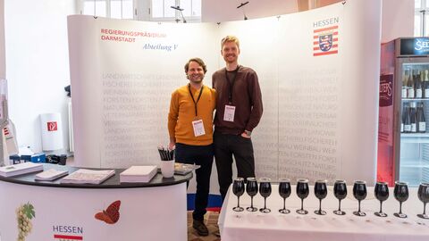 Mitarbeiter Maximilian Brückner (links) und Christian Ritzheim (rechts) am Stand des RP Zwei Männer stehen an einem weißen Stand