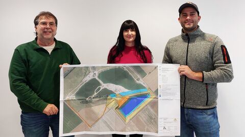 Eine Frau steht neben zwei Männern. Gemeinsam halten sie ein Plakat hoch, um es zu präsentieren.