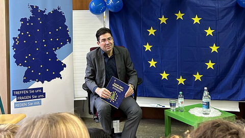 Regierungspräsident Prof. Dr. Jan Hilligardt im Klassenzimmer Person mit Buch in den Händen, hinter ihm eine Landkarte und eine EU-Flagge
