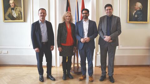 Staatsminister Kaweh Mansoori besucht das RP Darmstadt Drei Männer und eine Frau stehen nebeneinander. Sie schauen alle zur Kamera. Hinter ihnen sind drei Flaggen aufgestellt.