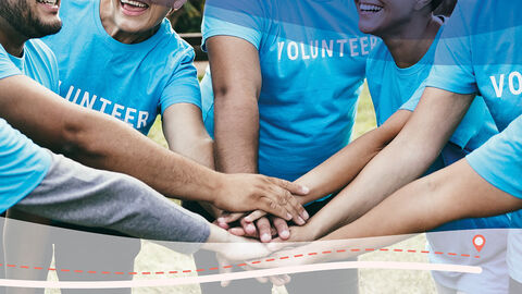Zusammenarbeit (Symbolbild) Junge Menschen in hellblauen T-Shirts, auf denen Volunteer steht, halten ihre Hände übereinander