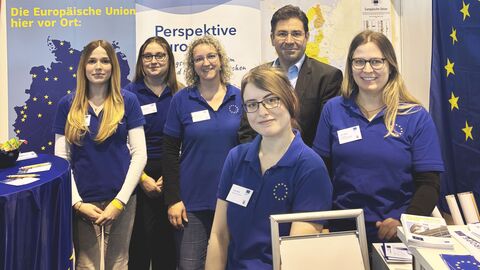 Berufswahlmesse Einstieg Fünf Frauen und ein Mann stehen nebeneinander an einem Stand auf einer Messe. Sie blicken alle in Richtung der Kamera