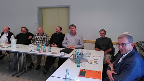 zahlreiche Personen sitzen um Tisch in Hufeisenform