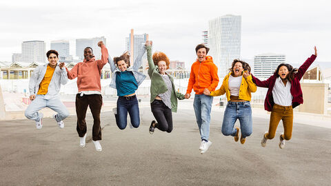 Sieben junge Menschen halten sich an den Händen und springen gleichzeitig nach oben