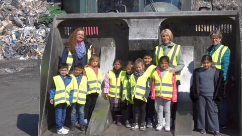 Mehrere Kinder und drei Erwachsene stehen in einer großen Baggeerschaufel