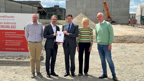 Fünf Personen auf Baustelle, im Hintergrund Hallen