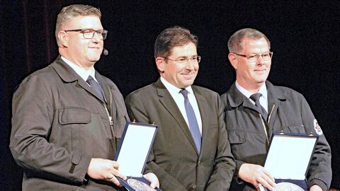 Drei Männer in schwarzen Anzügen mit Plaketten vor sich