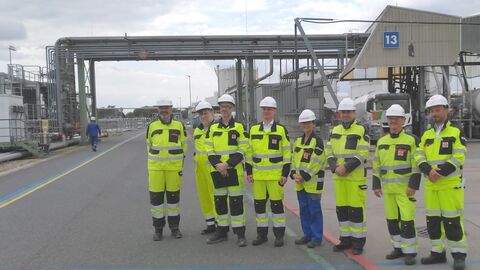 8 Personen in neongelben Anzügen auf Werksgelände