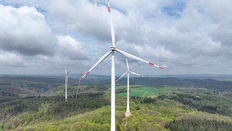 Mehrere Windräder auf bewaldetem Höhenzug, im Hintergrund Besiedelung
