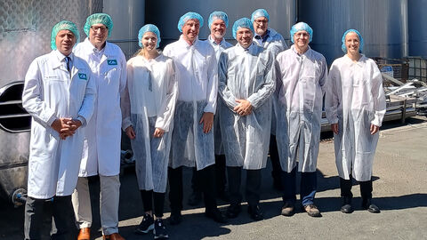 Neun Personen mit weißen Kitteln über ihrer Kleidung stehen nebeneinander vor großen Metallsäulen.