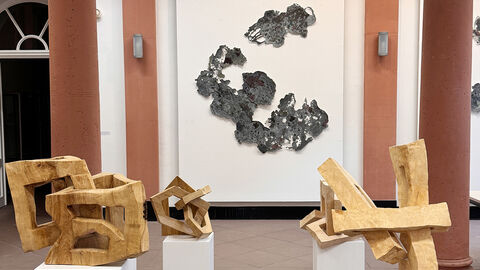 Mehrere Holzskulpturen stehen vor einer Wand mit einer Zeichnung