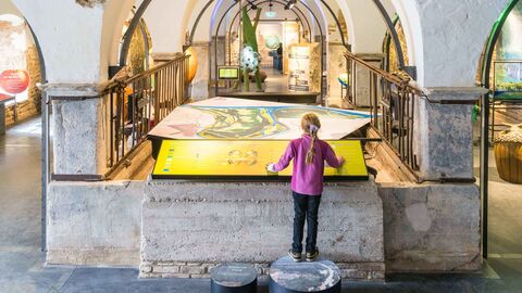 Kind steht in hohem Gewölbe und schaut auf großer Tafel vor ihm