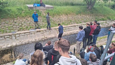 Personen stehen an begradigtem Bach