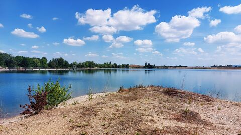 Eine mit Wassergefüllte Kiesgrube unter einem blauen Himmel.