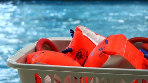 Mehrere Schwimmflügel liegen in einer kleinen Kiste. Im Hintergrund ist Wasser zu sehen.