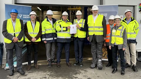 Acht Peronen stehen nebeneinander und schauen in die Kamera. Sieben von ihnen tragen eine gelbe Warnweste, eine Person eine orangene. In der Mitte halten zwei Männer gemeinsam eine Urkunde vor sich hoch.