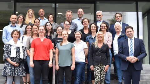 Eine Gruppe von Menschen steht auf einer Treppe und schaut in eine Kamera