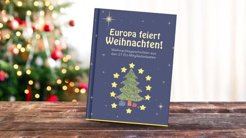 Weihnachtsbuch 2025 Das Weihnachtsbuch auf einem Tisch, ein Weihnachtsbaum im Hintergrund