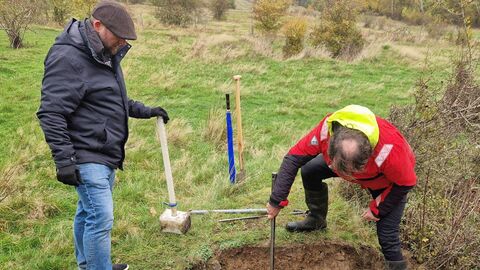 Zwei Männer hantieren an flacher Erdgrube