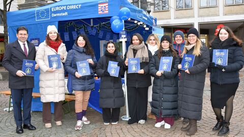 Eine Gruppe von Menschen steht in einer Reihe für ein Gruppenfoto bereit. Sie halten alle ein blaues Buch mit einem Tannenbaum darauf vor sich.