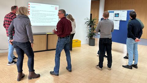 Einige Menschen stehen im Foyer eines Gebäudes. Sie schauen sich eine Präsentation an.