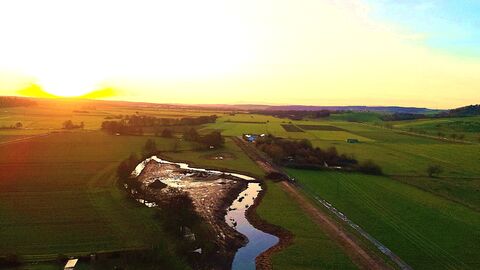 Totalaufnahme aus der Lut zeigt einen Bachverlauf bei Sonnenuntergang.
